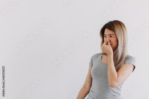Unhappy Asian Thai woman wear grey, squeezing, pinching and holding nose, blocking bad smell, looking at empty space smelly, isolated on white background wall. photo