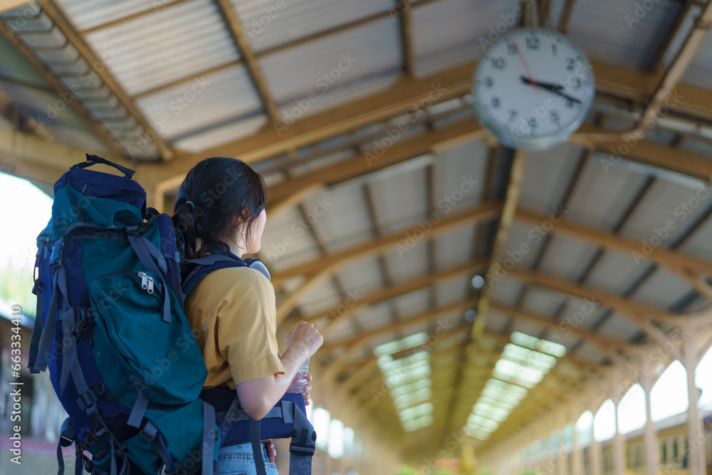Beautiful young Asian woman traveler looking clock over the head with a backpack, Waiting for the train at the train station, Travel, and vacation concept.