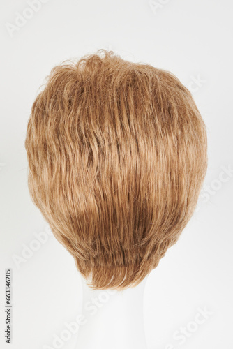 Natural looking blonde fair wig on white mannequin head. Short hair cut on the plastic wig holder isolated on white background  back view.