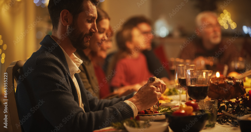 Portrait of Senior and Young Men and Women Sitting Together at a Cozy Christmas Dinner Celebration at Home. Everyone is Smiling and Enjoying a Festive Evening Meal in a Decorated Living Room