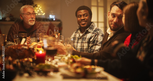 Portrait of a Handsome Young African Man Proposing a Toast at a Christmas Dinner Table. Family and Friends Sharing Meals, Raising Glasses with Champagne, Toasting, Celebrating a Winter Holiday