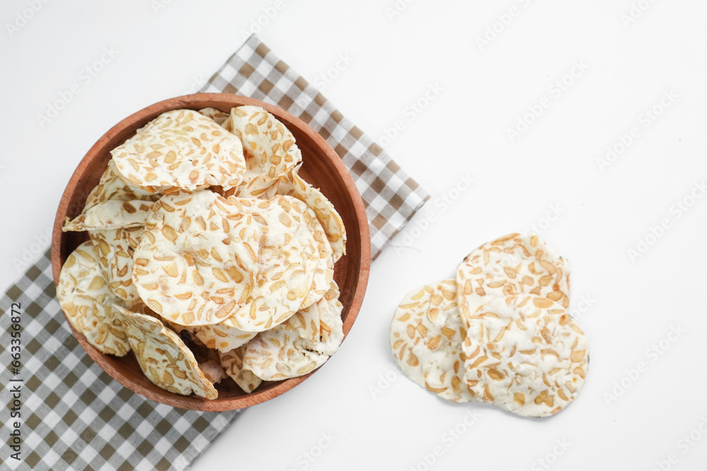 Keripik Tempe or Tempeh Chips are made from soybeans and served on a wooden plate. Isolated on white background.