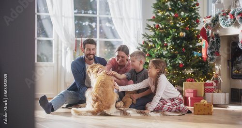 Portrait of Family at Home Sitting Next to a Christmas Tree, Petting Their Purebred Golden Retriever. Cute Pet Receiving a Lot of Love and Treats on Holiday. Family Bonding Together