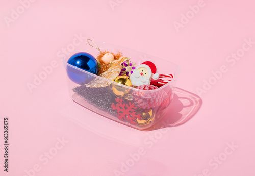 Bunch of Christmas ornaments packed in a plastic box on pink background. Minimal holiday decoration concept.