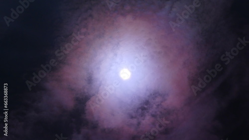 Dark night sky and moon with pink Lunar corona - abstract composition with optical phenomenon on clouds around moonlight. Topics: space, science, cosmos, atmosphere, weather