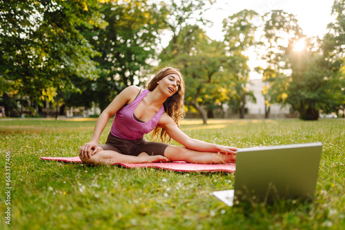 Happy woman in sportswear practicing fitness, online lesson with laptop. Active woman doing online training outdoors. Sports concept. Active lifestyle.