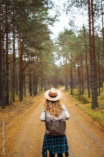 Beautiful woman in a hat with a backpack on a nature hike. A traveler walks in the autumn forest, enjoying the weather. Active lifestyle. © maxbelchenko