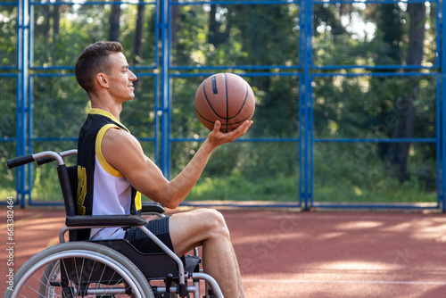 Happy basketball player with disability uses wheelchair while playing on outdoor sports court.