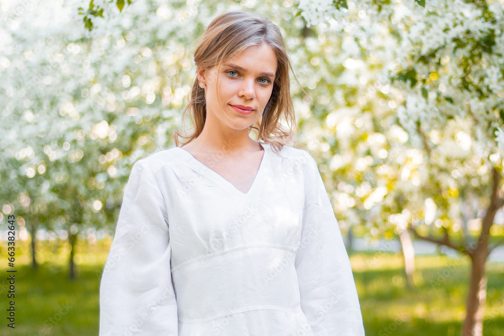 A young woman in a white dress walks against the backdrop of blooming apple trees. A girl posing against a background of flowers in a spring park. A young woman in a white dress walks against the backdrop of blooming apple trees. A girl posing against a background of flowers in a spring park.