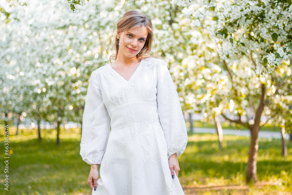 A young woman in a white dress walks against the backdrop of blooming apple trees. A girl posing against a background of flowers in a spring park. A young woman in a white dress walks against the backdrop of blooming apple trees. A girl posing against a background of flowers in a spring park.