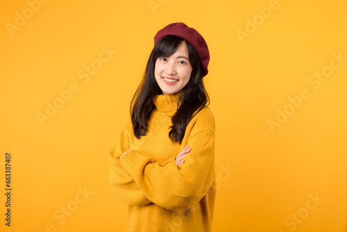 Cool young Asian woman in her 30s, with arms crossed on her chest, exuding a stylish vibe in a yellow sweater and red beret against a yellow background.