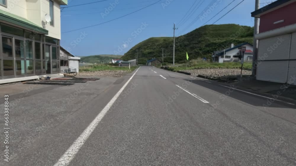 Riding past houses and sheds on Rebun Island coastal road on sunny day Riding past houses and sheds on Rebun Island coastal road on sunny day
