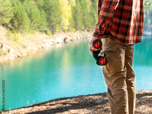 unrecognizable man tourist dressed in red plaid shirt, engaged in birdwatching with binoculars on the banks of calm blue mountain lake in the autumn forest A haven for nature enthusiasts copy space