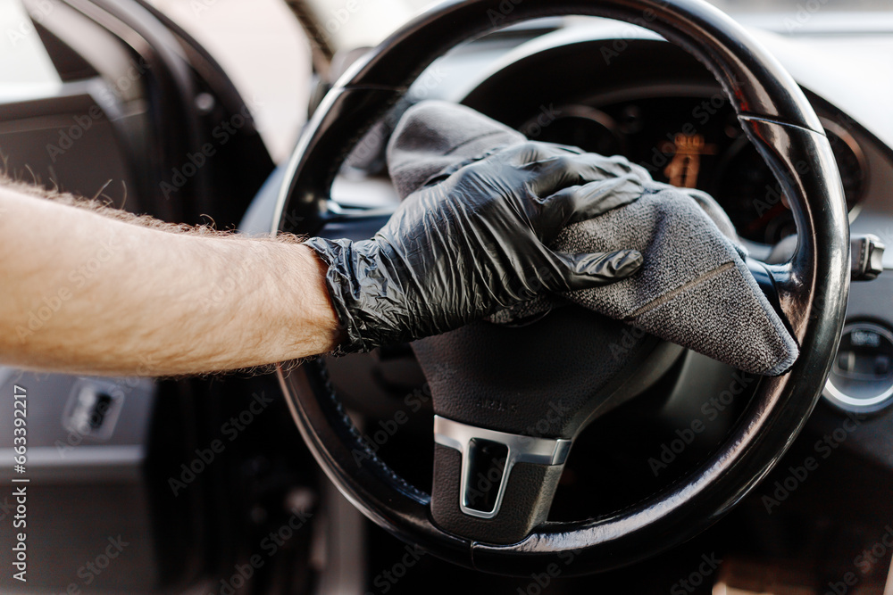 Man's hand in black glove cleaning car interior, dashboard and leather seats with microfiber cloth. Hand wipe down suede leather seat saloon interior.