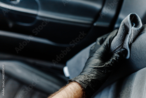 Man s hand in black glove cleaning car interior  dashboard and leather seats with microfiber cloth. Hand wipe down suede leather seat saloon interior.