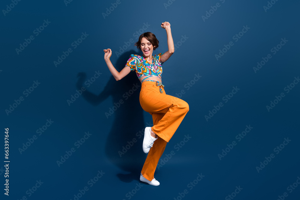 Full body photo of pretty young girl raise fists celebrate winning wear trendy flared pants outfit isolated on dark blue color background Full body photo of pretty young girl raise fists celebrate winning wear trendy flared pants outfit isolated on dark blue color background