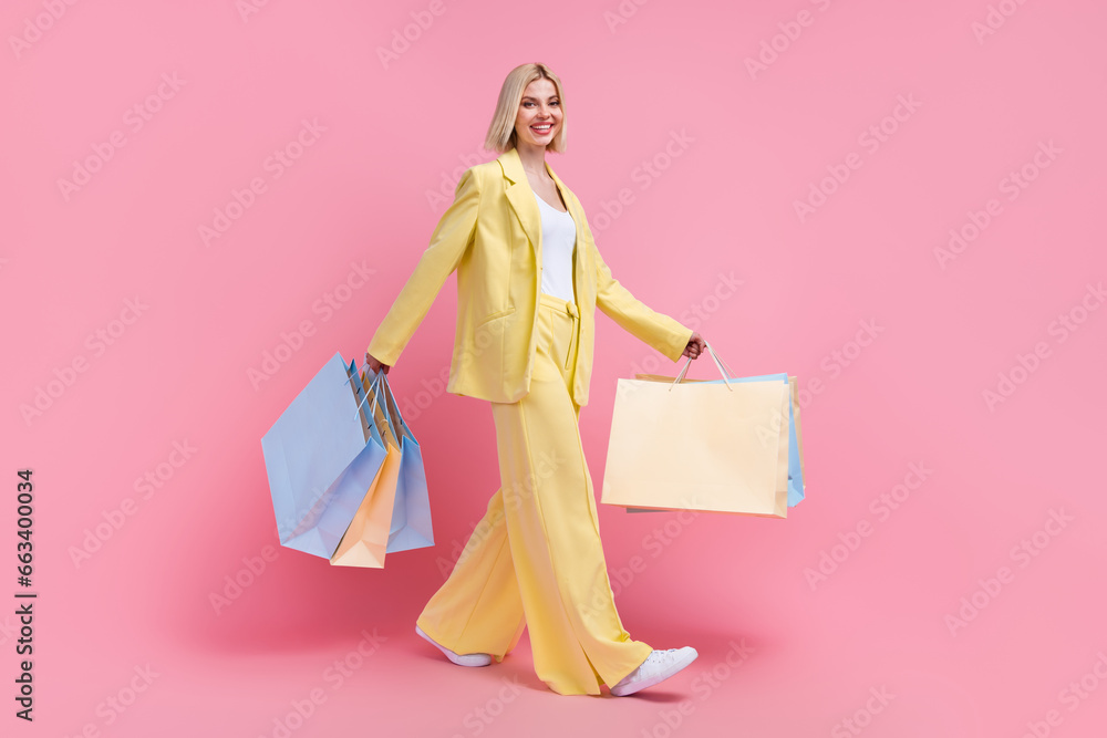 Full length profile photo of stunning cheerful person hold store bags walking isolated on pink color background Full length profile photo of stunning cheerful person hold store bags walking isolated on pink color background