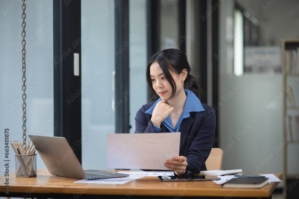Asian woman working with document papers and laptop sitting at desk workplace office. Asian woman working with document papers and laptop sitting at desk workplace office.