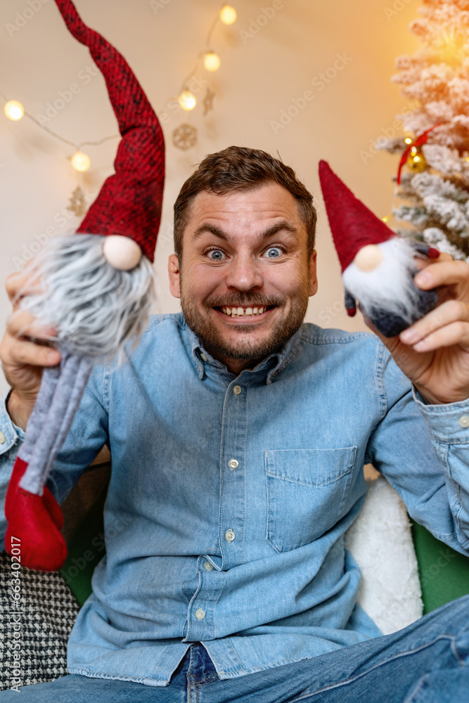 Obraz premium Childishness of adult people while Christmas. Young adult happy man playing with kids toy gnomes.