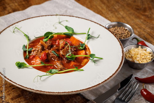 Beef goulash with tomato and arugula on wooden background