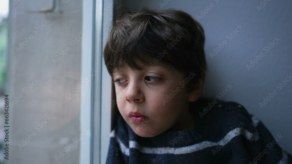 Sad pensive child looking out from home window with thoughtful bored expression. Close-up little boy confined at residence Sad pensive child looking out from home window with thoughtful bored expression. Close-up little boy confined at residence