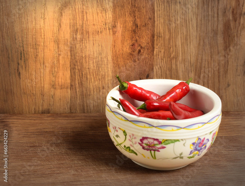 Pods of hot red pepper in a light bowl on a wooden background