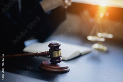 Lawyer woman holding a law book with a wooden legal gavel on an office desk, justice and law concept.