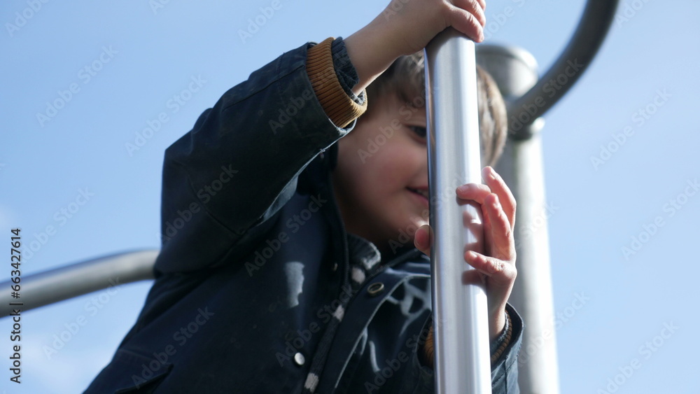 Joyful child sliding down metal bar at playground structure. Fun little boy enjoying outdoor exercise in childhood, wearing jacket during autumn day