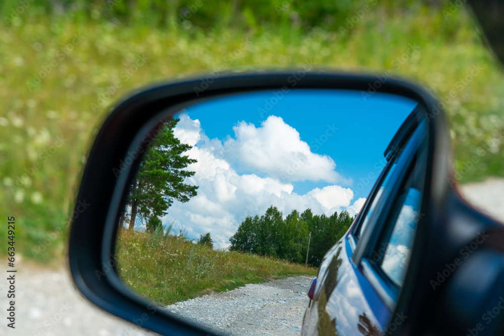 Summer countryside landscape in the rearview mirror of a car during a trip