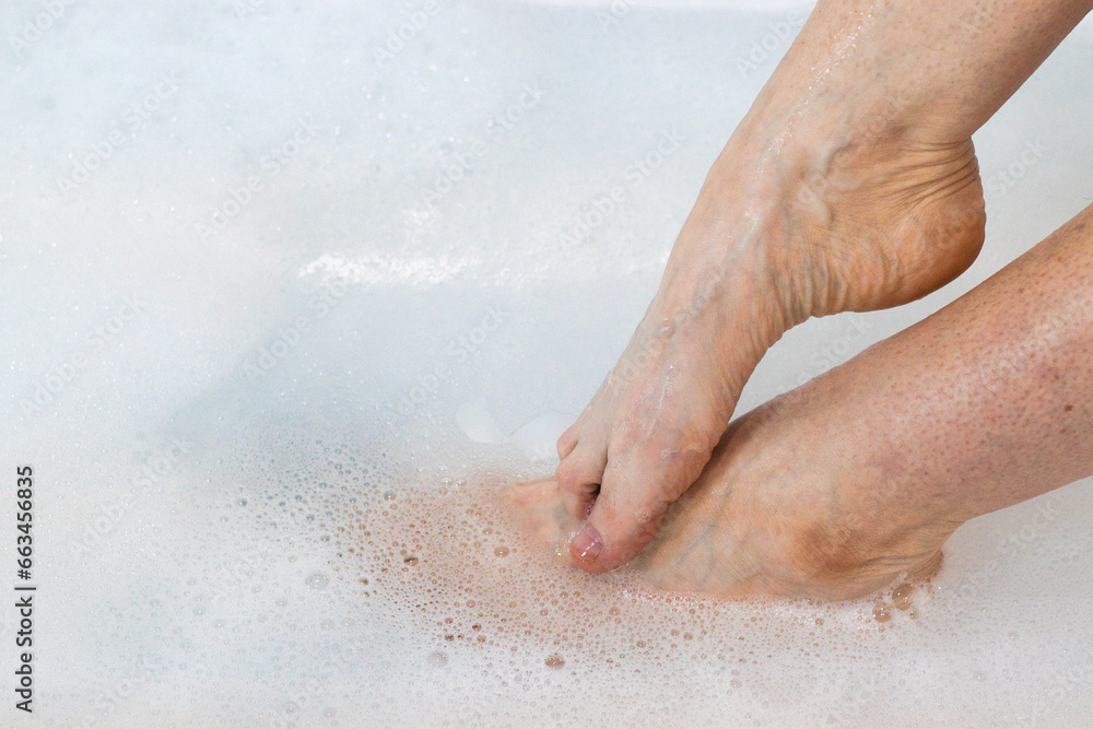 One foot on top of the other in a tub of water with bubbles. One foot on top of the other in a tub of water with bubbles.