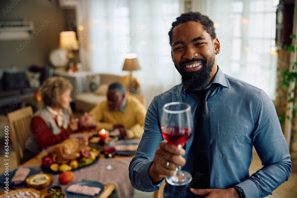 Happy black man toasting during family gathering on Thanksgiving and looking at camera.