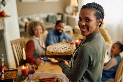 Happy black woman serving Thanksgiving pie to her family and looking at camera.