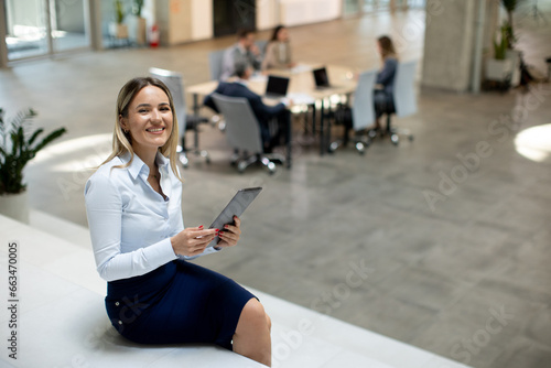 Young woman with digital tablet standing in the modern office in front of her team