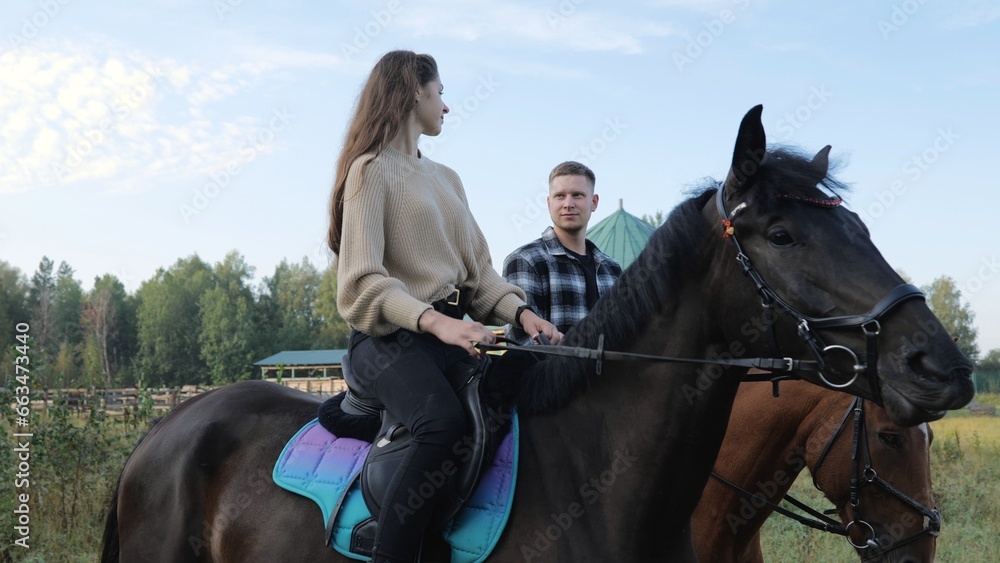 Obraz premium Training hobby during the holidays. Horseback riding at the farm, equestrian club. A young family rides horses. Riding lessons, a young couple ride horses in a paddock at a ranch.