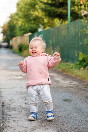 Caucasian baby child girl walks on wet asphalt and smiles