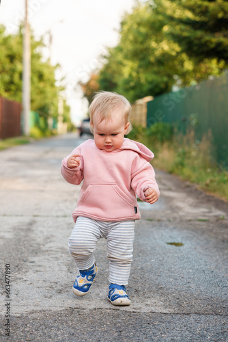 Caucasian baby child girl walks on wet asphalt and smiles