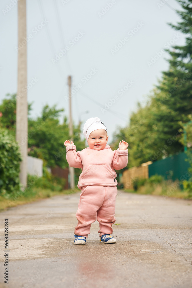 Caucasian baby child girl walks on wet asphalt and smiles