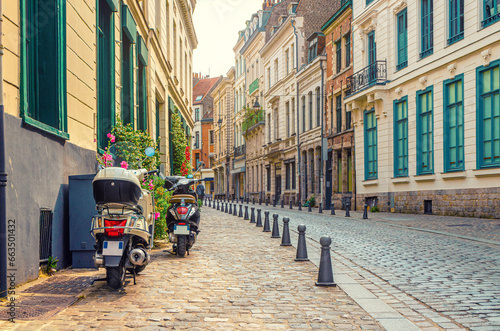Two scooters bikes parked on empty narrow cobblestone street  paving stone road  old colorful buildings with stone walls in Lille old town historical city centre  French Flanders  Northern France