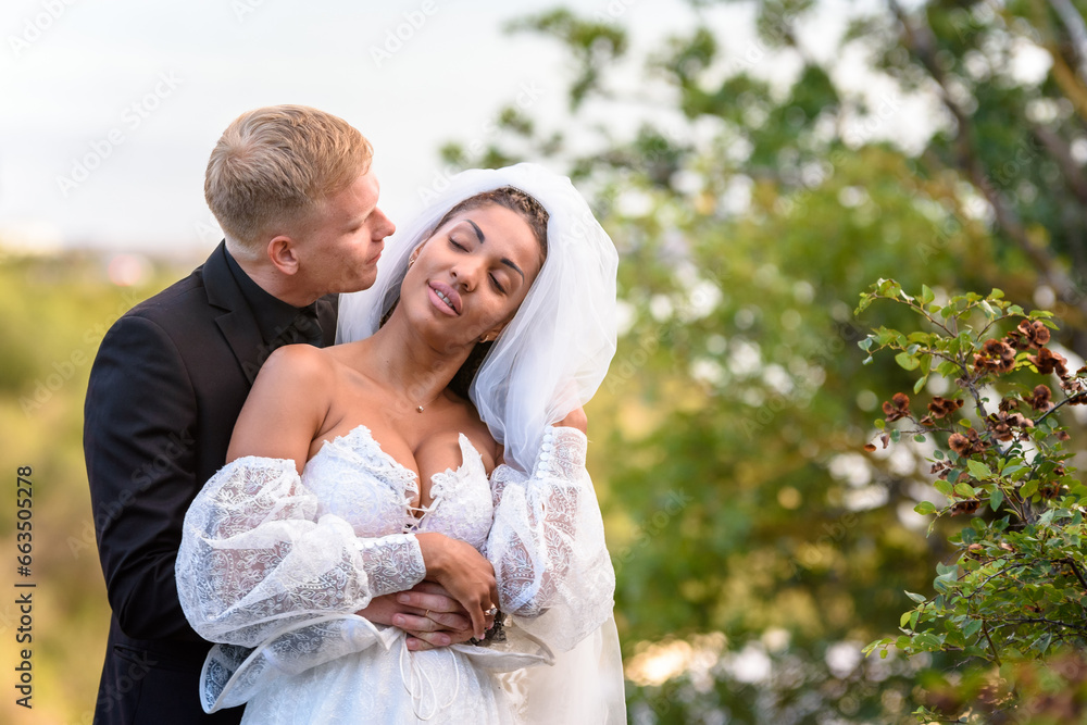 Happy newlyweds hug against the backdrop of a beautiful mountain landscape, the guy kisses the girl who has closed her eyes Happy newlyweds hug against the backdrop of a beautiful mountain landscape, the guy kisses the girl who has closed her eyes