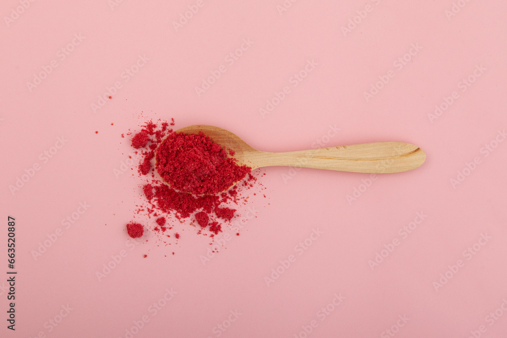 Dried raspberries powder in wooden spoon on pink background. Dehydrated fruits in powder are often added to drinks, cocktails, smoothies and porridges for breakfast - obrazy, fototapety, plakaty 