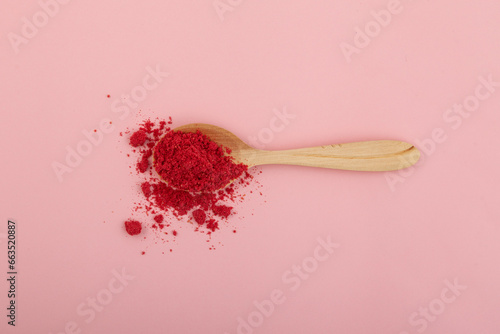Dried raspberries powder in wooden spoon on pink background. Dehydrated fruits in powder are often added to drinks, cocktails, smoothies and porridges for breakfast