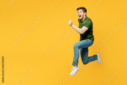 Full body side profile view young sporty cool fun happy man he wearing green t-shirt casual clothes jump high run fast hurry up isolated on plain yellow background studio portrait. Lifestyle concept. photo