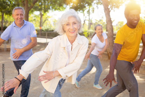 Group of various aged mixed-race adult people exercising and performing sports activities at park on sunny day