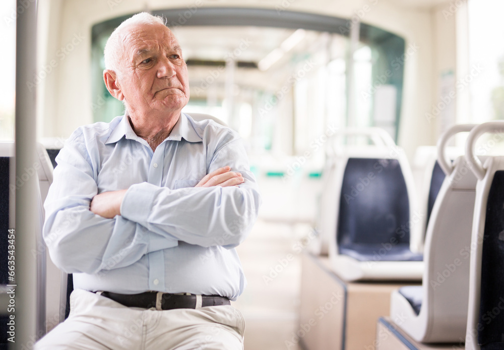 Fototapeta premium Senior European man sitting on seat inside tram and waiting for his stop.