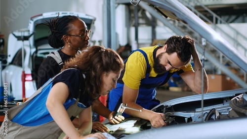 Photos Team of technicians in car service using inspection lamp to fix damaged automobile