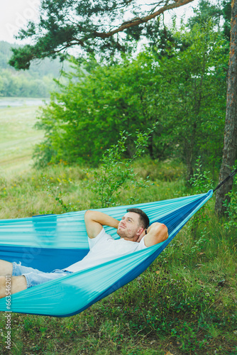 A young man rests in nature sitting in a tourist hammock. Hammock for outdoor recreation. Weekend rest of a lonely man in a deserted forest © Дмитрий Ткачук