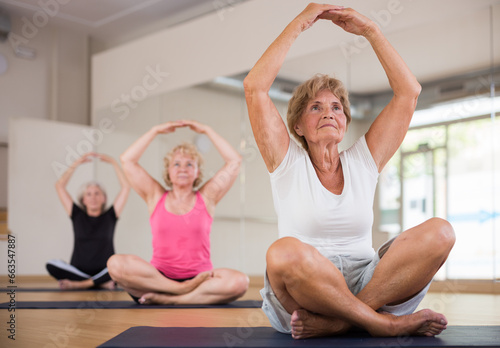 Group of active aged women practicing yoga in a fitness studio train in the lotus position