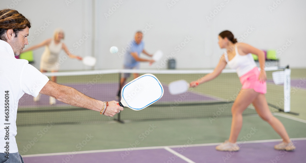 White paddle-shaped racquet for pickleball in hand of male player swinging to hit ball during friendly match in close court, selective focus..