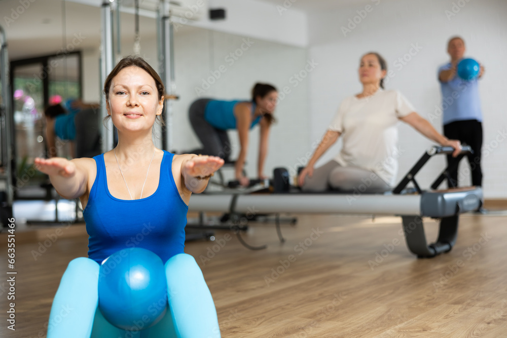 Young woman performing sit-up with bender ball to strengthen abdominal muscles during group pilates class in fitness studio