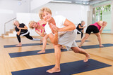 Group of three aged women standing in yoga pose in fitness room.